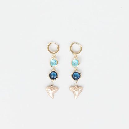 Pair of earrings with gold hoops, blue gemstones, and real gold fossil shark teeth on a white background.