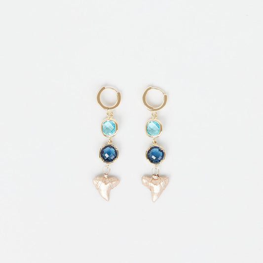 Pair of earrings with gold hoops, blue gemstones, and real gold fossil shark teeth on a white background.